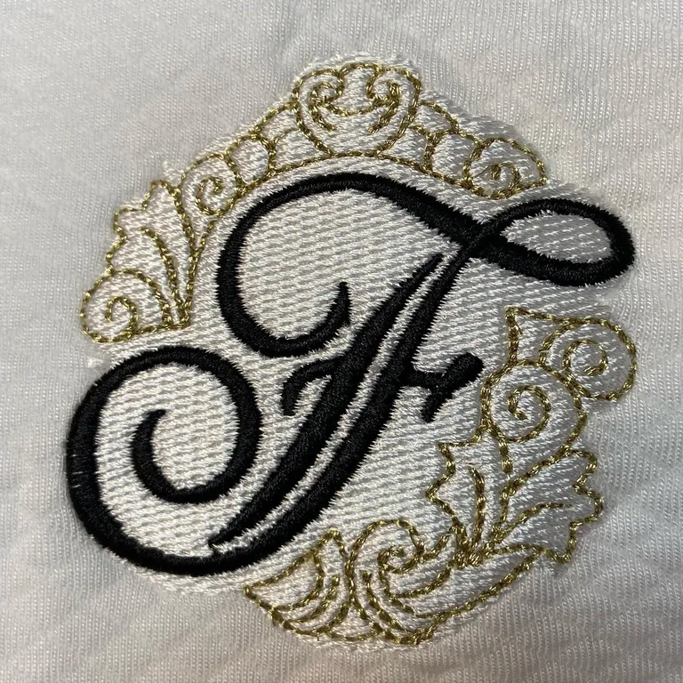 Close-up of a black script monogram with metallic gold filigree embroidered on white fabric