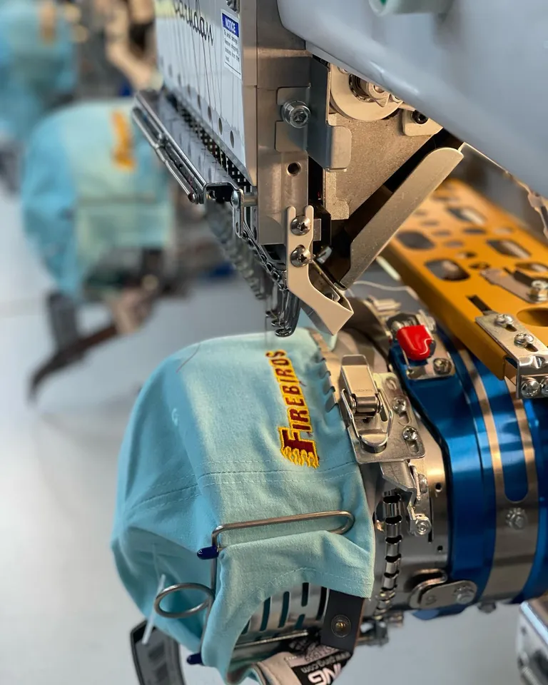 Barudan embroidery machine stitching a red and gold Firebirds logo on a light blue cap at Edge Embroidery in Scottsdale