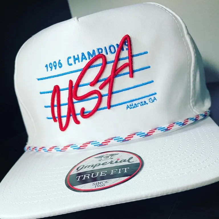 White rope-brim hat with red 3D puff USA script and blue 1996 Champions lettering